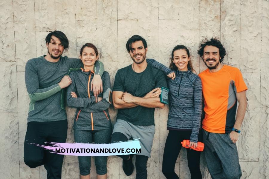 Five smiling young adults stand in front of a textured, light-colored wall, dressed in athletic wear. One man has an arm around the shoulder of the woman beside him, and another woman has an arm around the shoulder of the man beside her. One man wears a smartphone armband. A water bottle is in one woman’s hand. A motivational website’s watermark overlays the bottom.