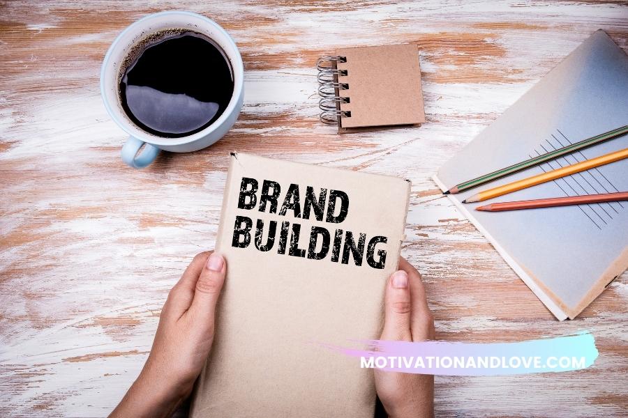 Hands holding a book titled "Brand Building," atop a distressed wooden surface with a cup of coffee, a small notebook, and lined paper with pencils.