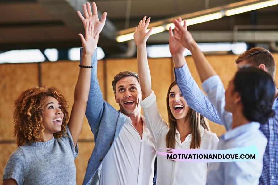 Group of five diverse colleagues with arms raised, smiling in a bright modern office.