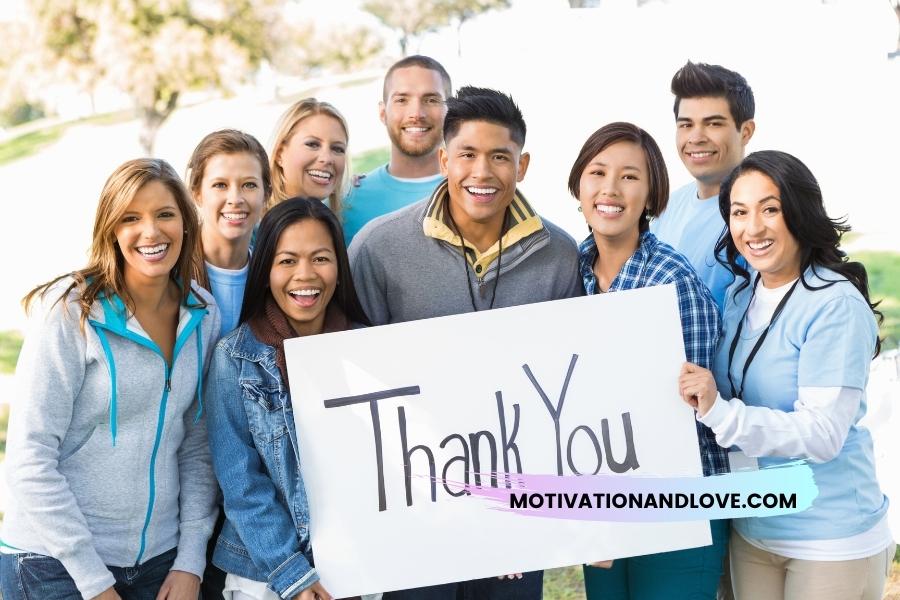 Group of smiling people holding a sign that reads "Thank You" with the URL motivationandlove.com.